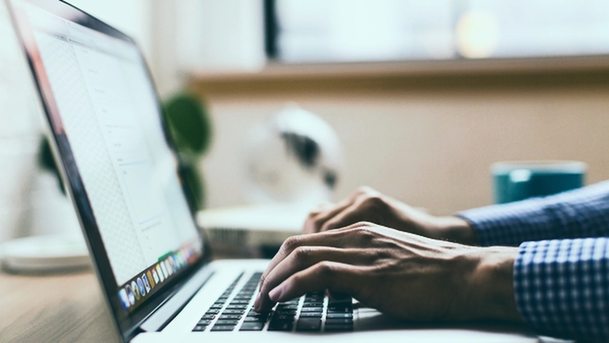 Mãos digitando em laptop com documentos de escritório ao redor